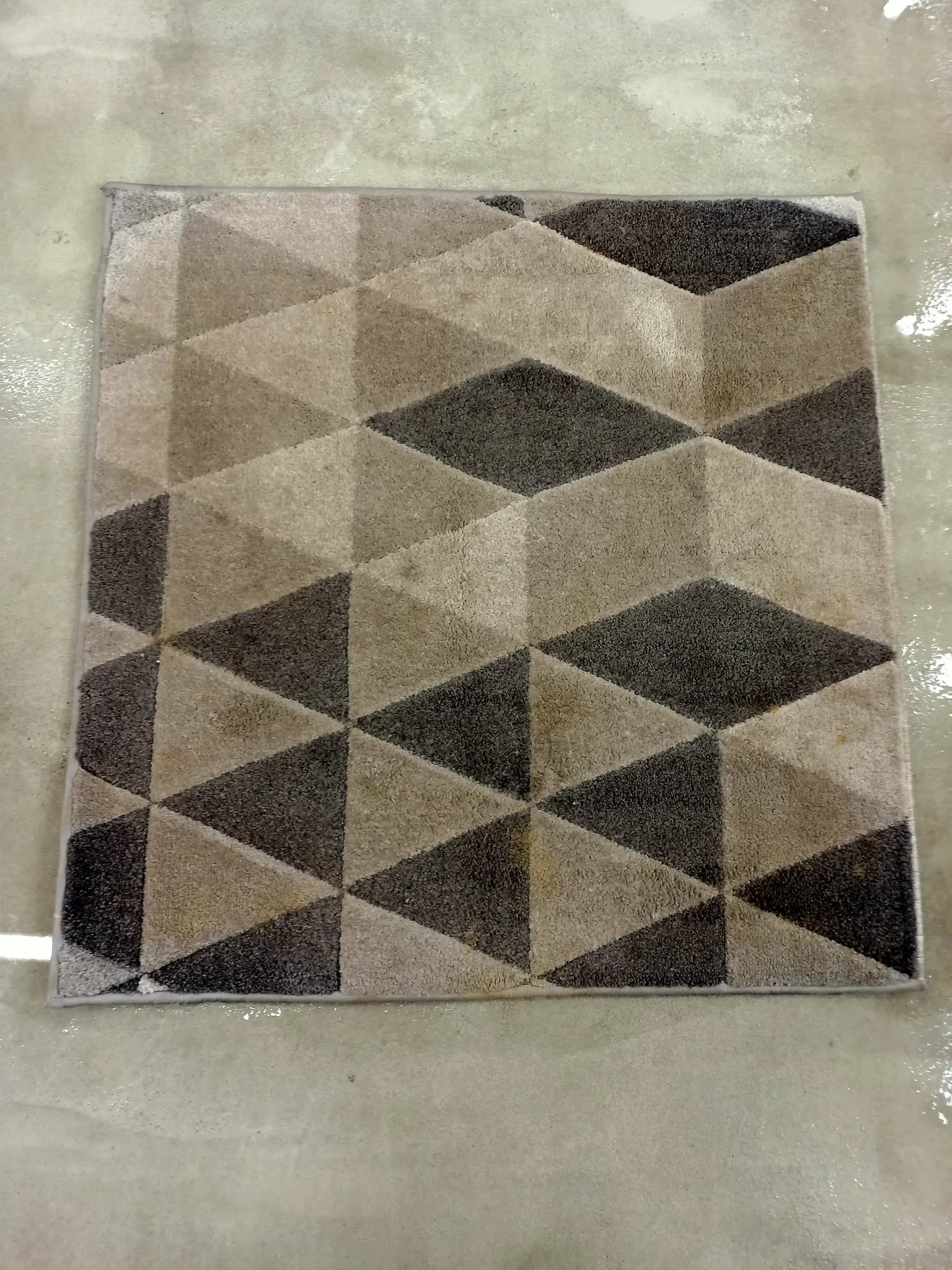 Zabrudzony dywan w geometryczne wzory, w brunatnych odcieniach.