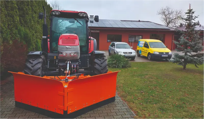 widok na sprzęt firmy, ciągnik z pługiem oraz 3 samochody, w tle widok siedziby